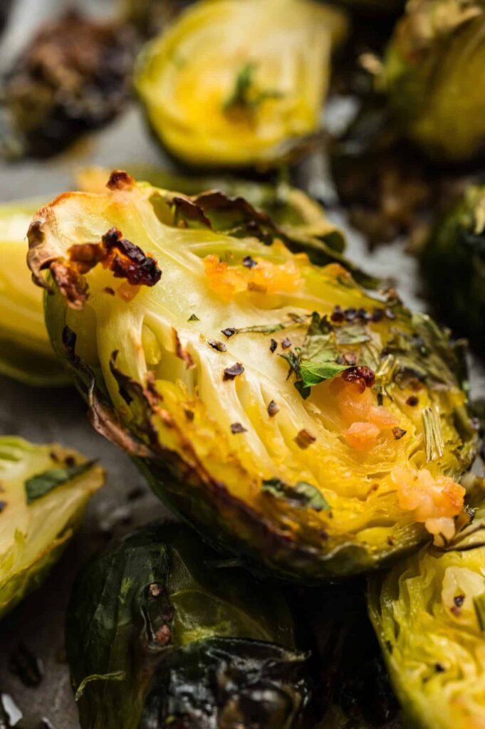 Close-up of a crispy oven roasted Brussels sprout half, golden brown with garlic, herbs, and caramelized edges.