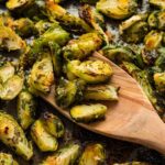 Golden brown oven roasted Brussels sprouts with garlic and herbs, served on a baking sheet with a wooden spoon.
