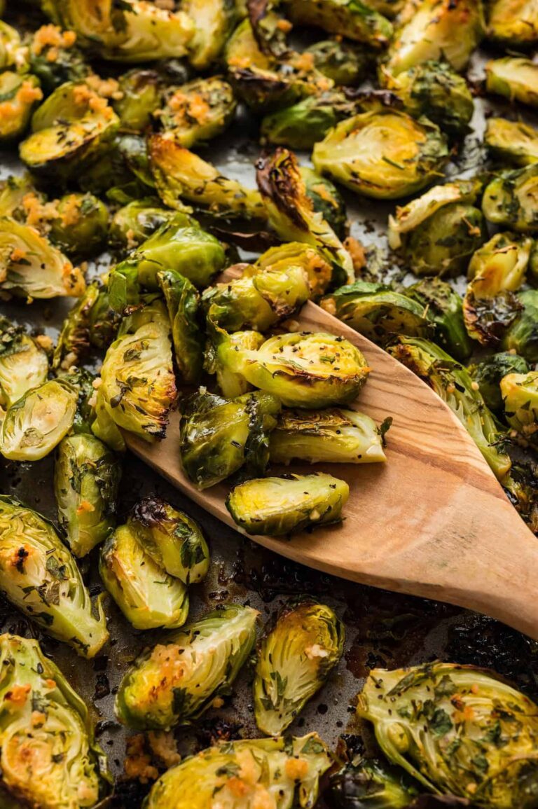 Golden brown oven roasted Brussels sprouts with garlic and herbs, served on a baking sheet with a wooden spoon.