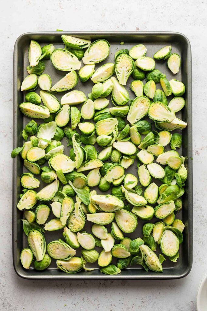 Baking sheet with fresh halved Brussels sprouts spread out evenly, ready for seasoning and roasting.