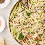 Bowl of creamy apple coleslaw made with shredded cabbage, carrots, and crisp green apples, garnished with fresh cilantro.