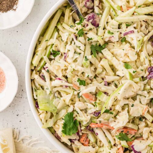 Bowl of creamy apple coleslaw made with shredded cabbage, carrots, and crisp green apples, garnished with fresh cilantro.