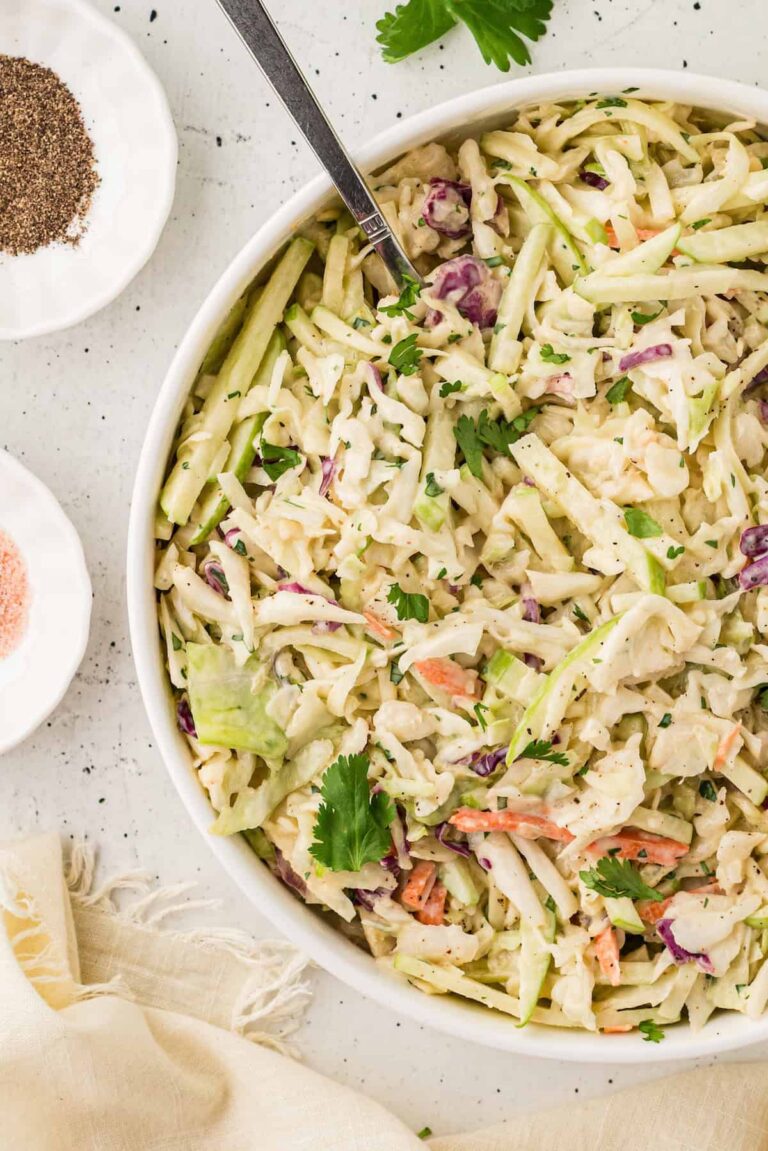 Bowl of creamy apple coleslaw made with shredded cabbage, carrots, and crisp green apples, garnished with fresh cilantro.
