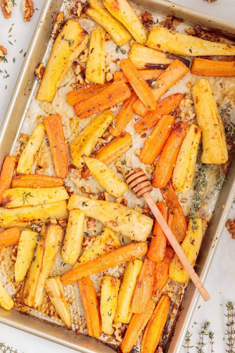 Golden roasted carrot and parsnip sticks on a parchment-lined baking sheet, sprinkled with toasted walnuts and fresh thyme, with a honey dipper resting on top for a touch of sweetness.