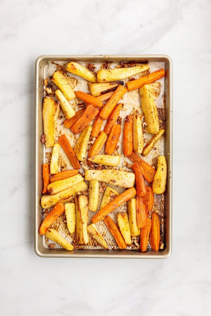 Golden roasted carrots and turnips on a parchment-lined baking sheet, caramelized around the edges with toasted walnuts scattered throughout