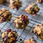 Close-up of no-bake peanut butter protein balls with chocolate chips, granola, dried cranberries, and pepitas cooling on a wire rack.