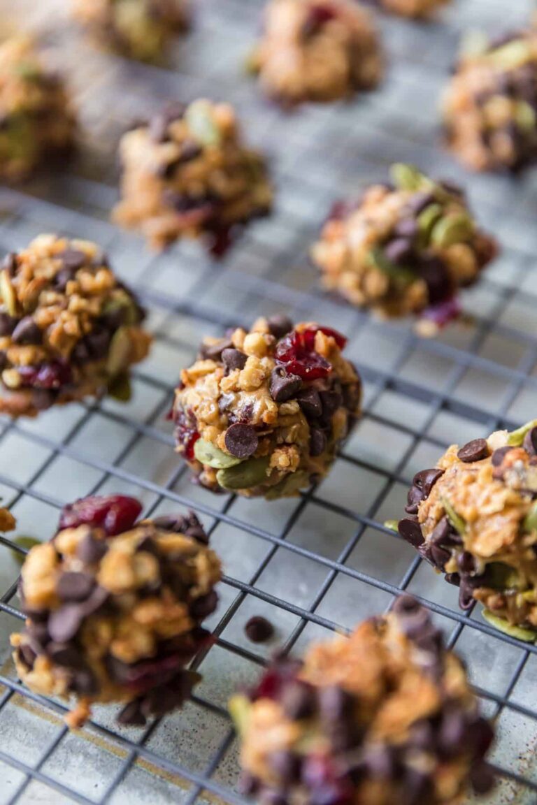 Close-up of no-bake peanut butter protein balls with chocolate chips, granola, dried cranberries, and pepitas cooling on a wire rack.