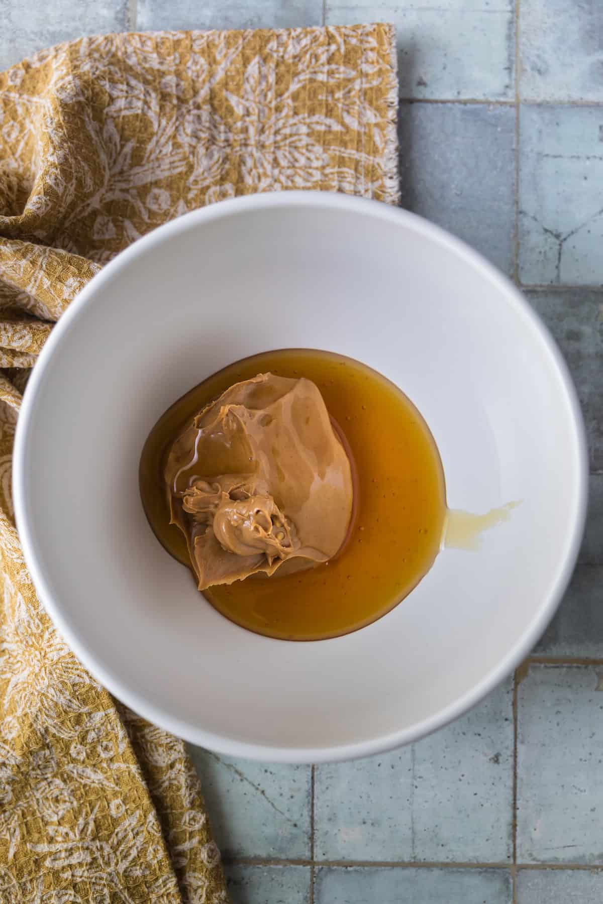 Peanut butter and honey in a white bowl, the base ingredients for homemade no-bake peanut butter balls (protein energy bites).