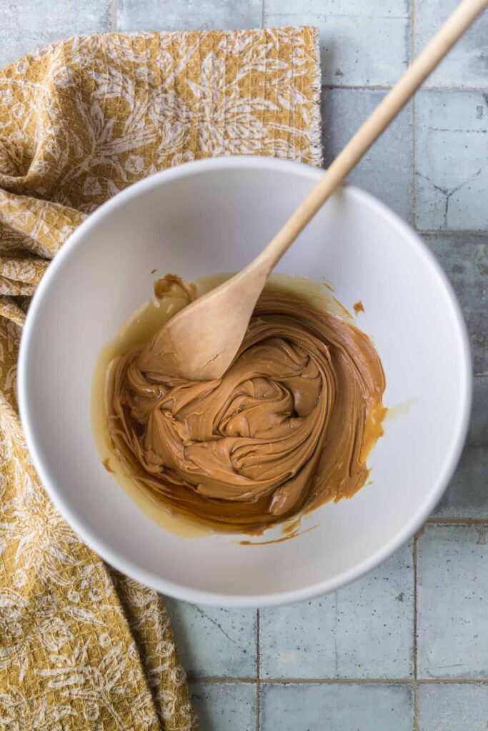 Peanut butter and honey being stirred together in a mixing bowl with a wooden spoon until smooth and creamy.