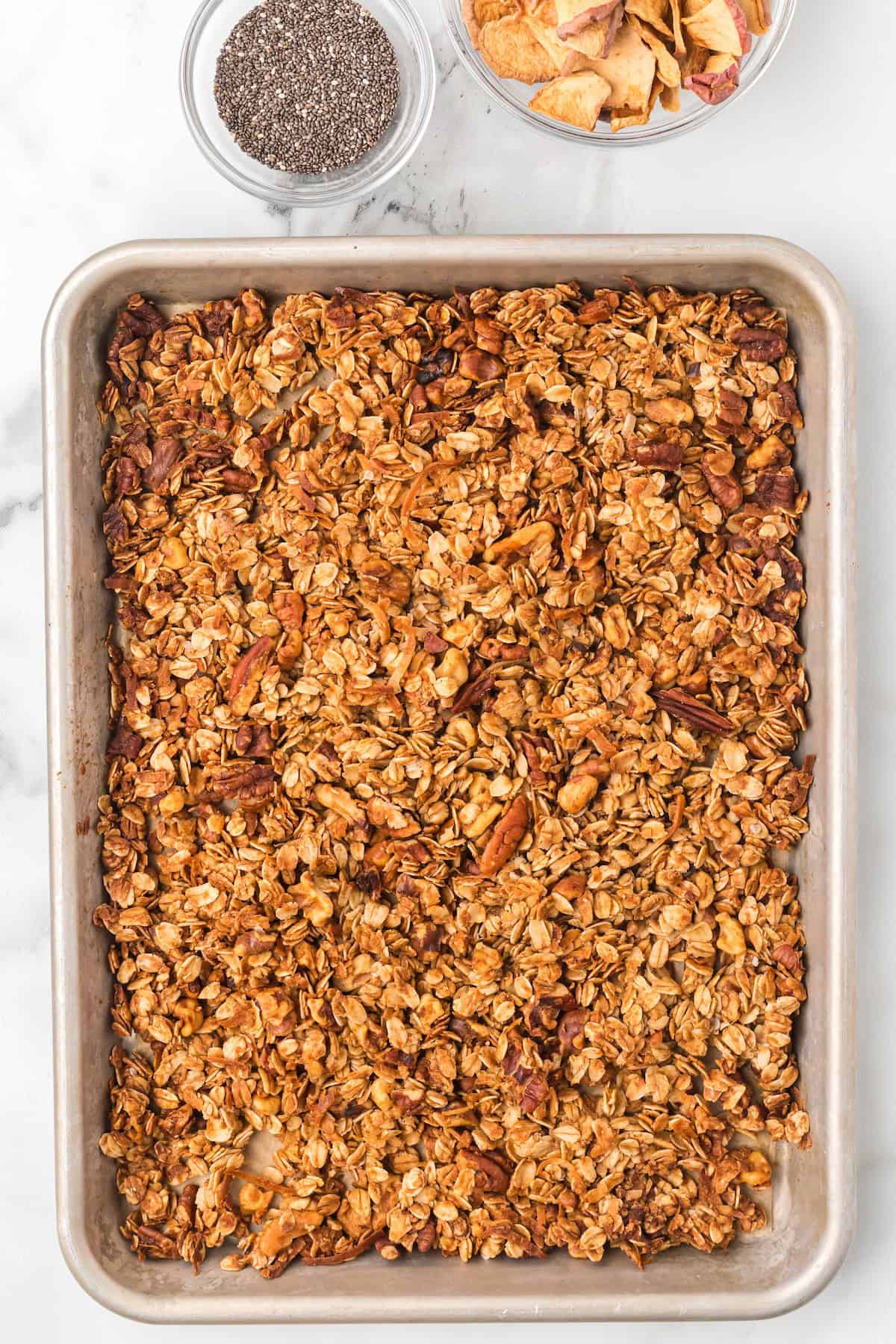 Golden homemade apple pie granola with oats, pecans, walnuts, and dried apples cooling on a baking sheet.