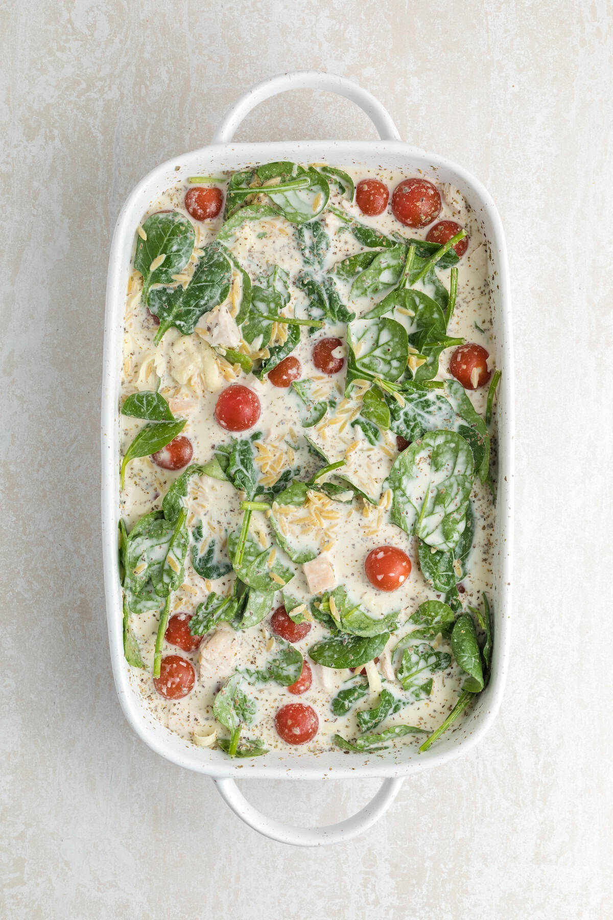 One-pan creamy chicken orzo mixture with spinach and cherry tomatoes combined in a white baking dish, ready to bake.
File name: creamy-chicken-orzo-ready-to-bake.jp