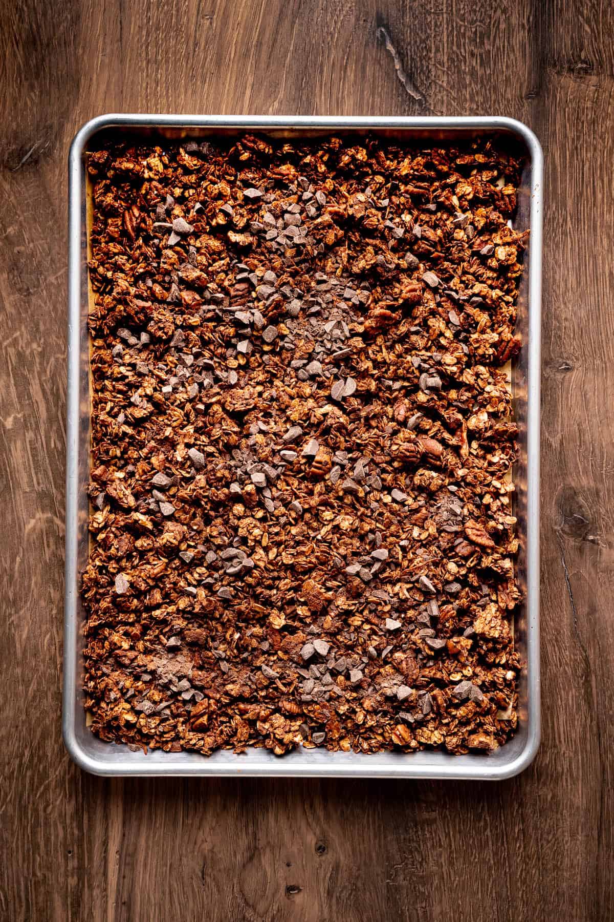 Baking sheet filled with homemade chocolate coconut granola topped with dark chocolate chunks after cooling.