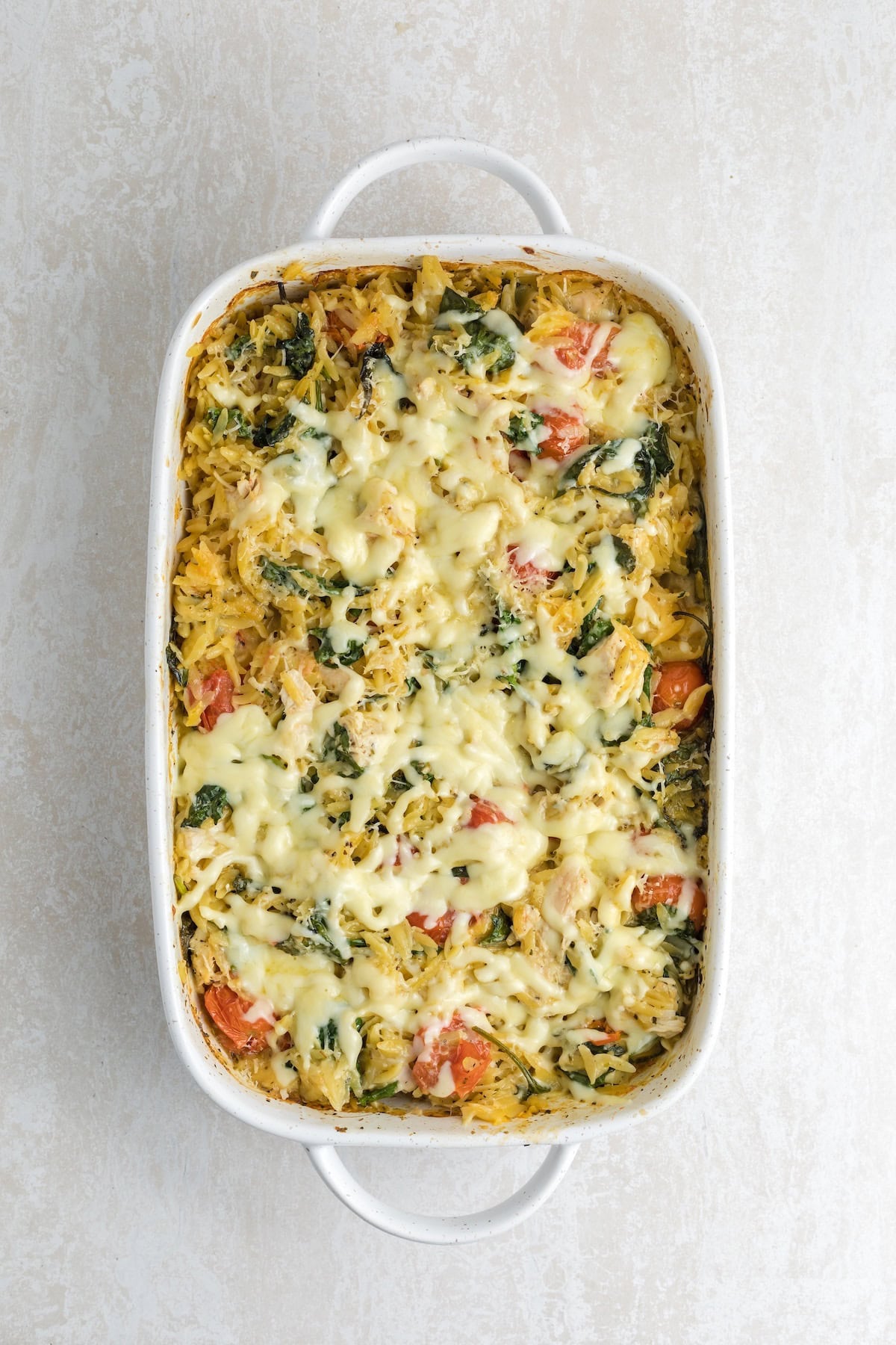 Golden, cheesy one-pan chicken orzo bake with spinach and tomatoes, showing a creamy texture and bubbly melted cheese on top.