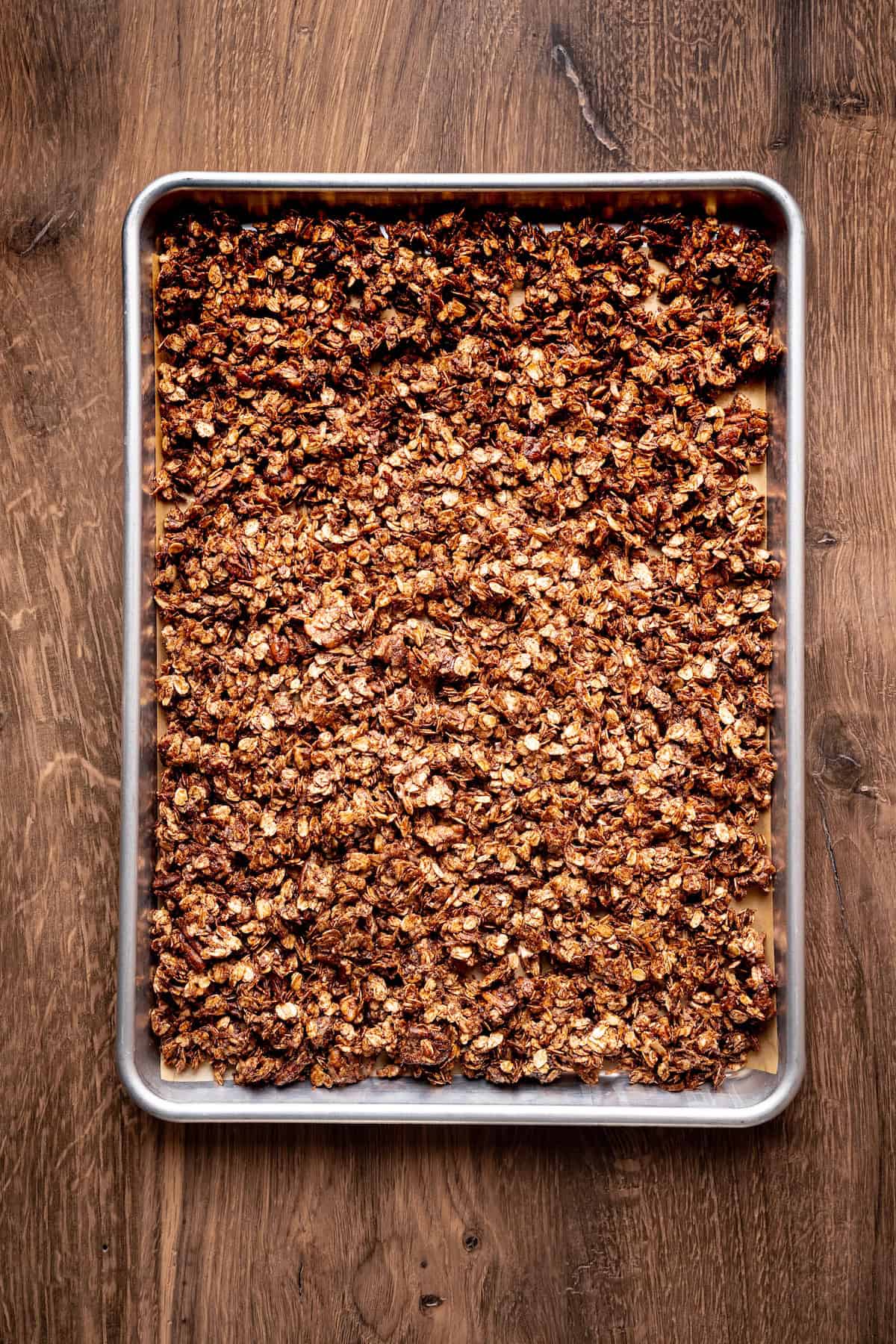 Baking sheet lined with parchment paper topped with an even layer of chocolate coconut granola mixture spread out before baking.