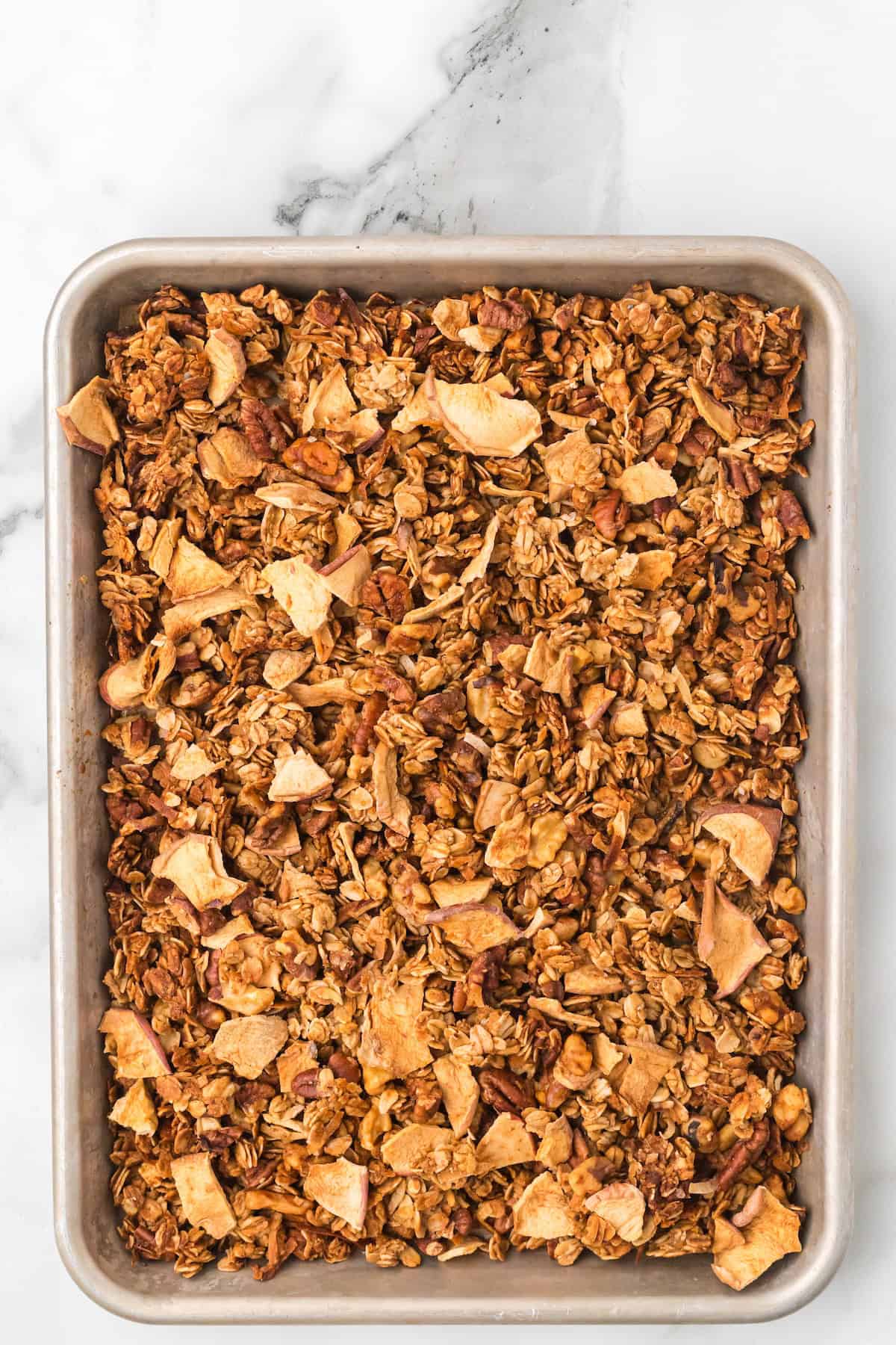 Unbaked apple pie granola mixture made with oats, pecans, and coconut spread evenly on a baking sheet, ready to bake into golden clusters.