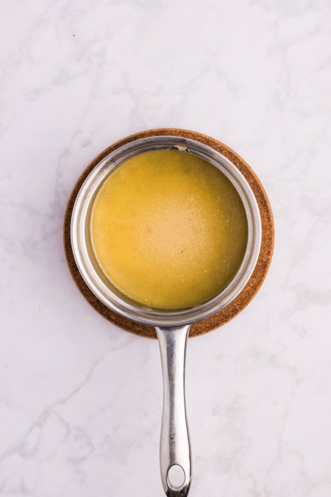 Small saucepan filled with golden homemade gravy made from herb roasted chicken pan drippings, resting on a cork trivet over a marble surface.