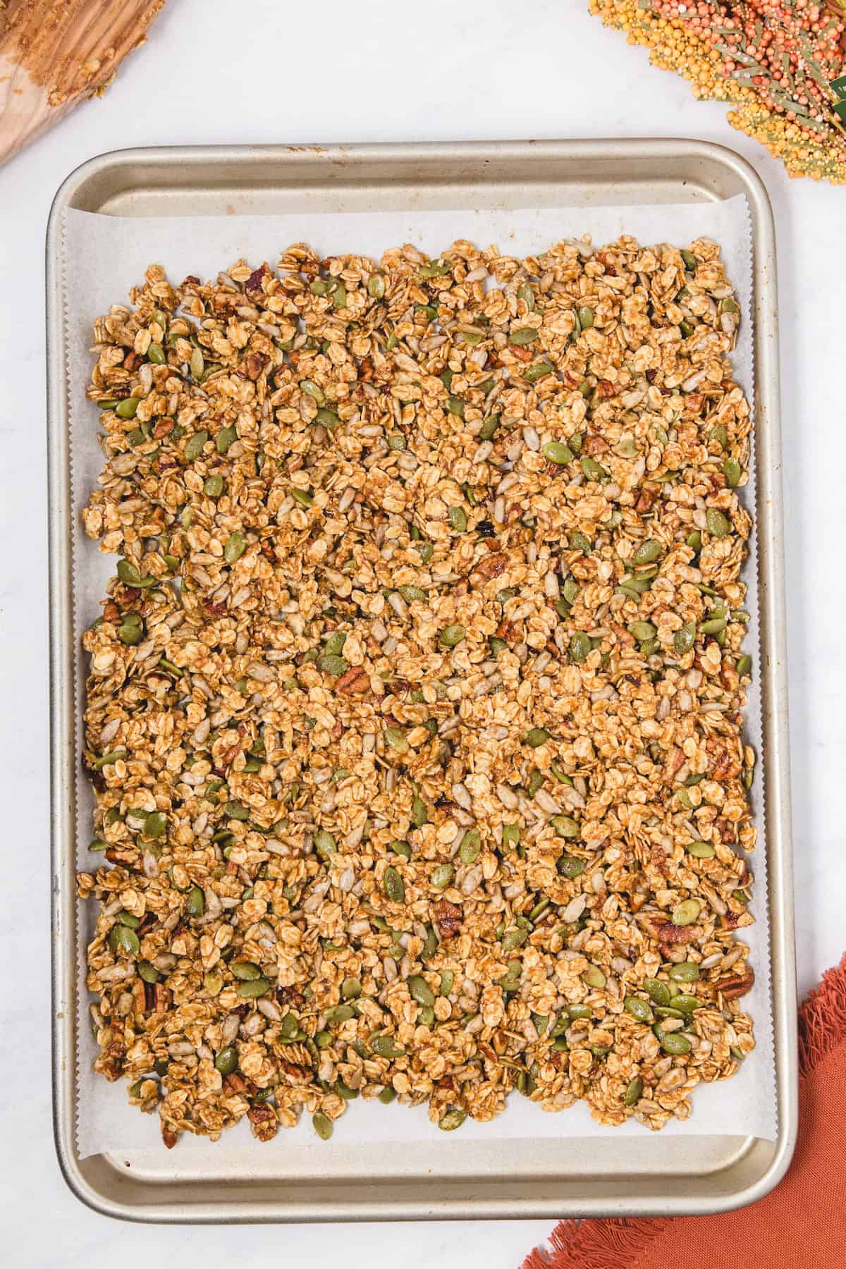 Baking sheet lined with parchment paper covered in an even layer of pumpkin spice granola made with oats, seeds, and pecans, ready to be baked until golden and crunchy.