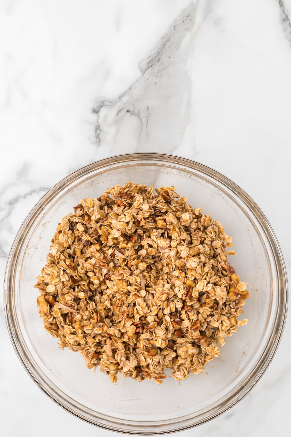 Granola mixture of oats, nuts, and coconut fully coated with maple syrup and applesauce, ready to bake into crunchy apple pie granola.