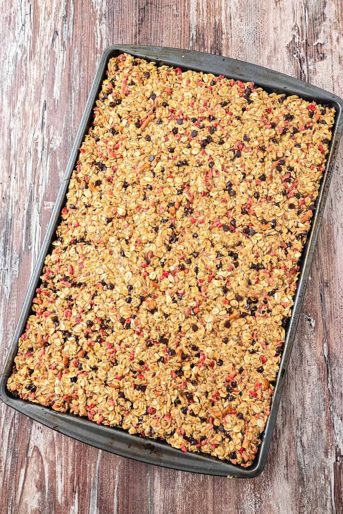 No bake homemade chewy granola bars pressed into a parchment-lined baking sheet before chilling.