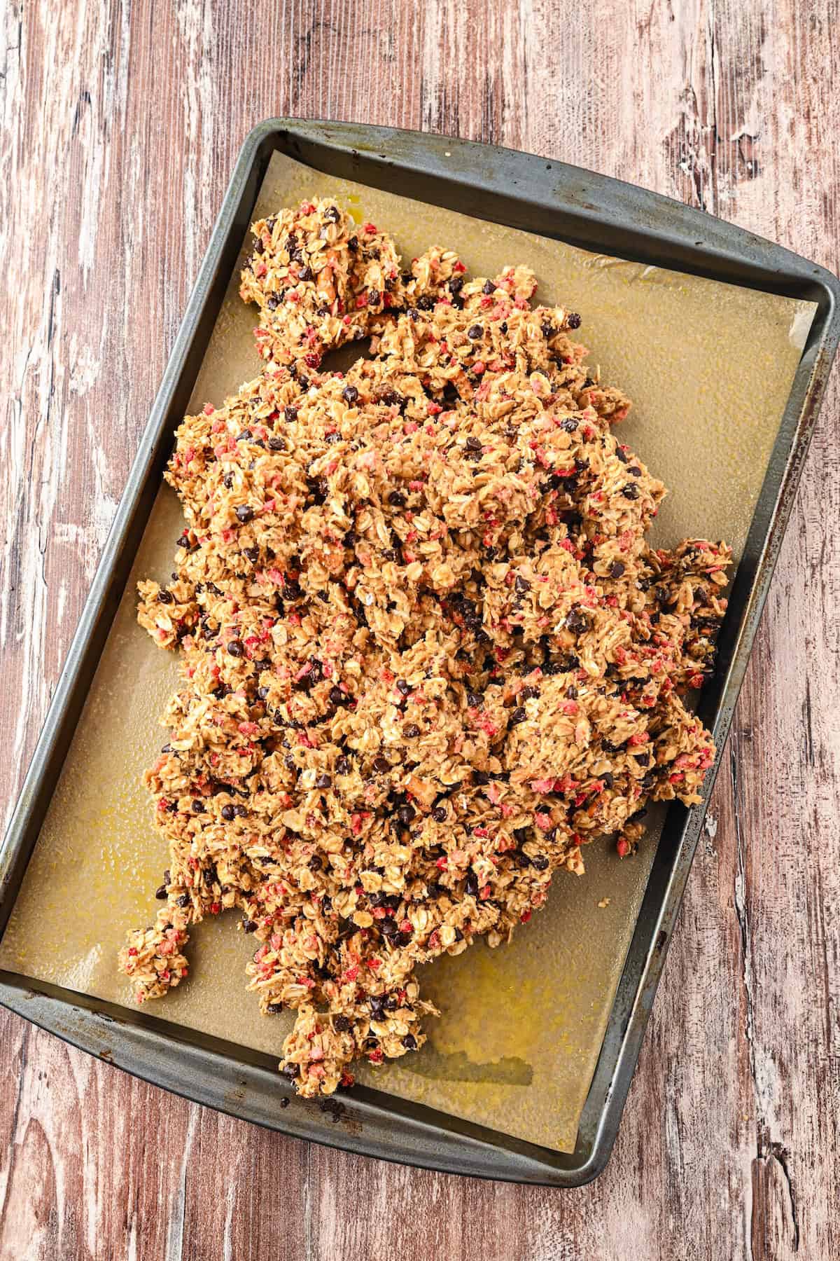 No bake homemade chewy granola bar mixture spread onto a parchment-lined baking sheet before pressing.