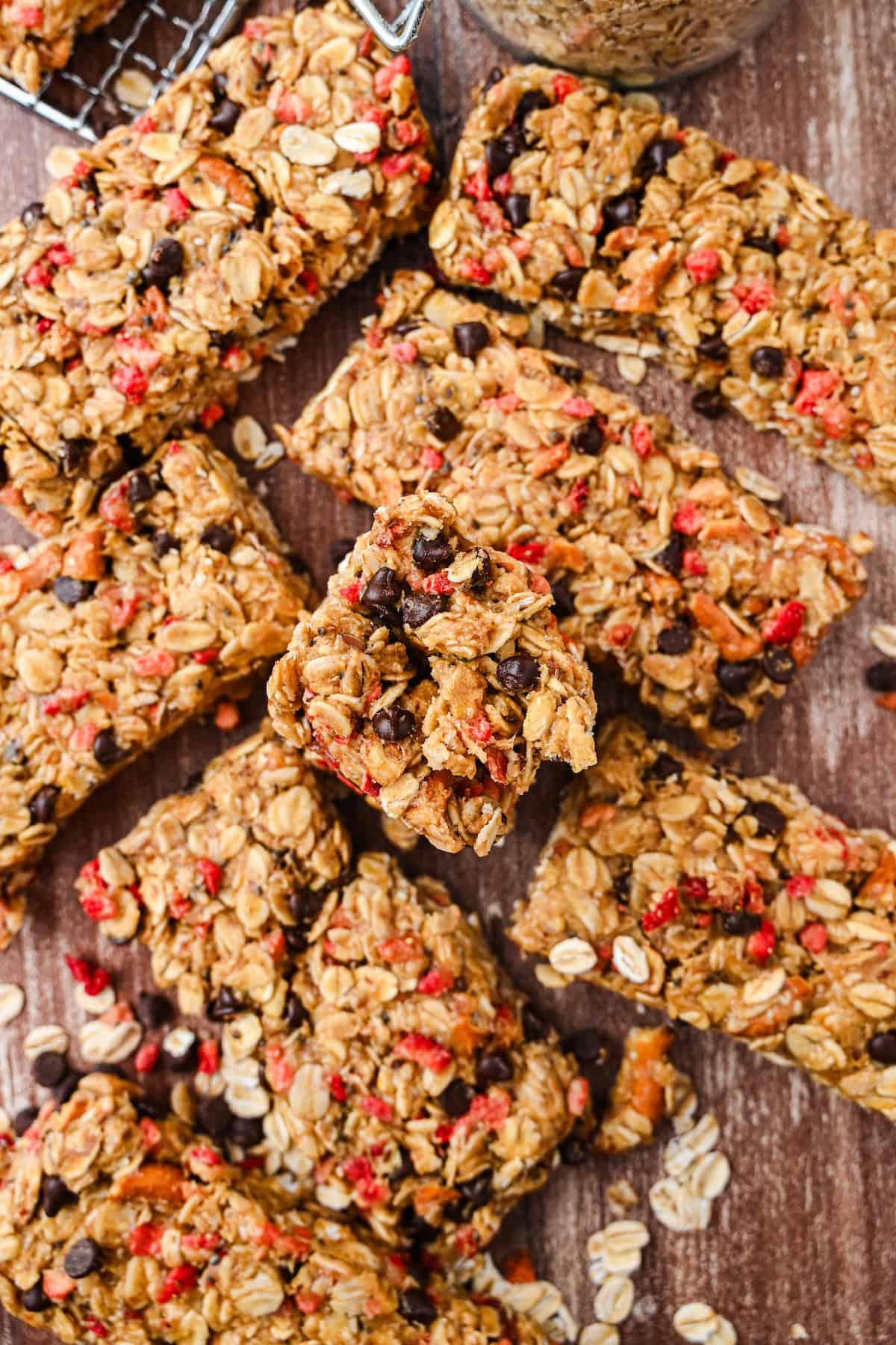 Homemade chewy granola bars made with oats, peanut butter, honey, chocolate chips, and freeze-dried strawberries arranged on a wooden surface.