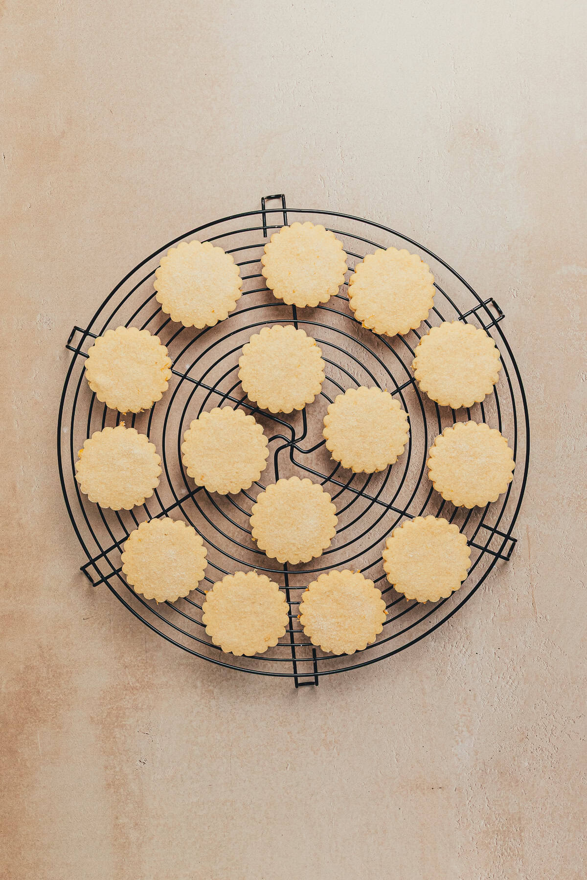 Freshly baked lemon cookies cooling on a wire rack with scalloped edges.