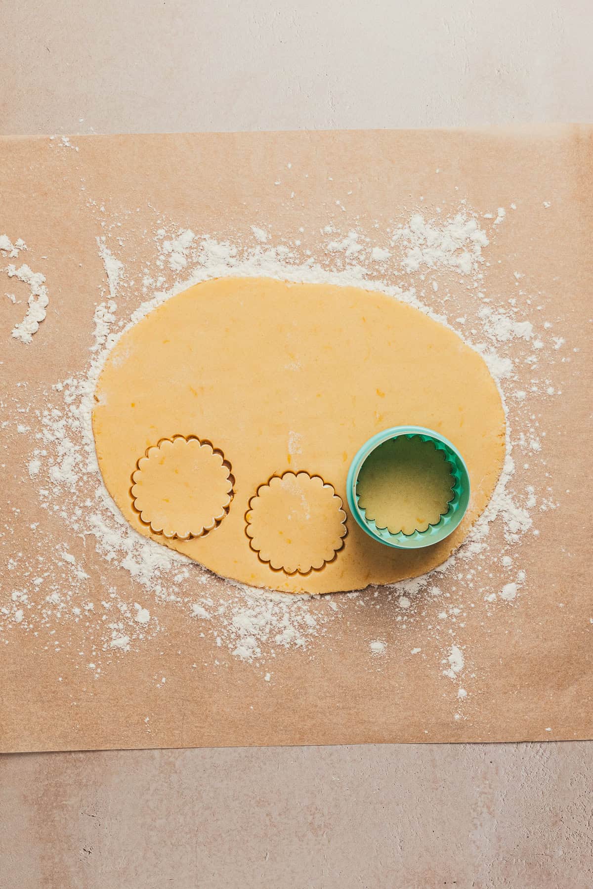 Scalloped cookie cutters cutting lemon sandwich cookies from rolled dough on parchment paper.