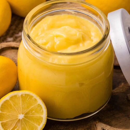 Homemade Instant Pot lemon curd in a glass jar with fresh lemons.