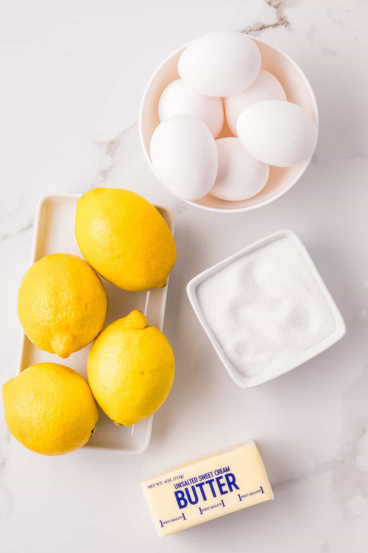 Ingredients for Instant Pot lemon curd including fresh lemons, eggs, sugar, and butter on a marble countertop.