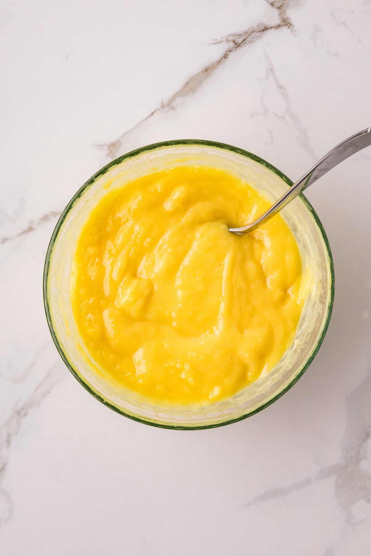 Creamy homemade Instant Pot lemon curd in a glass bowl with a spoon on a marble countertop.