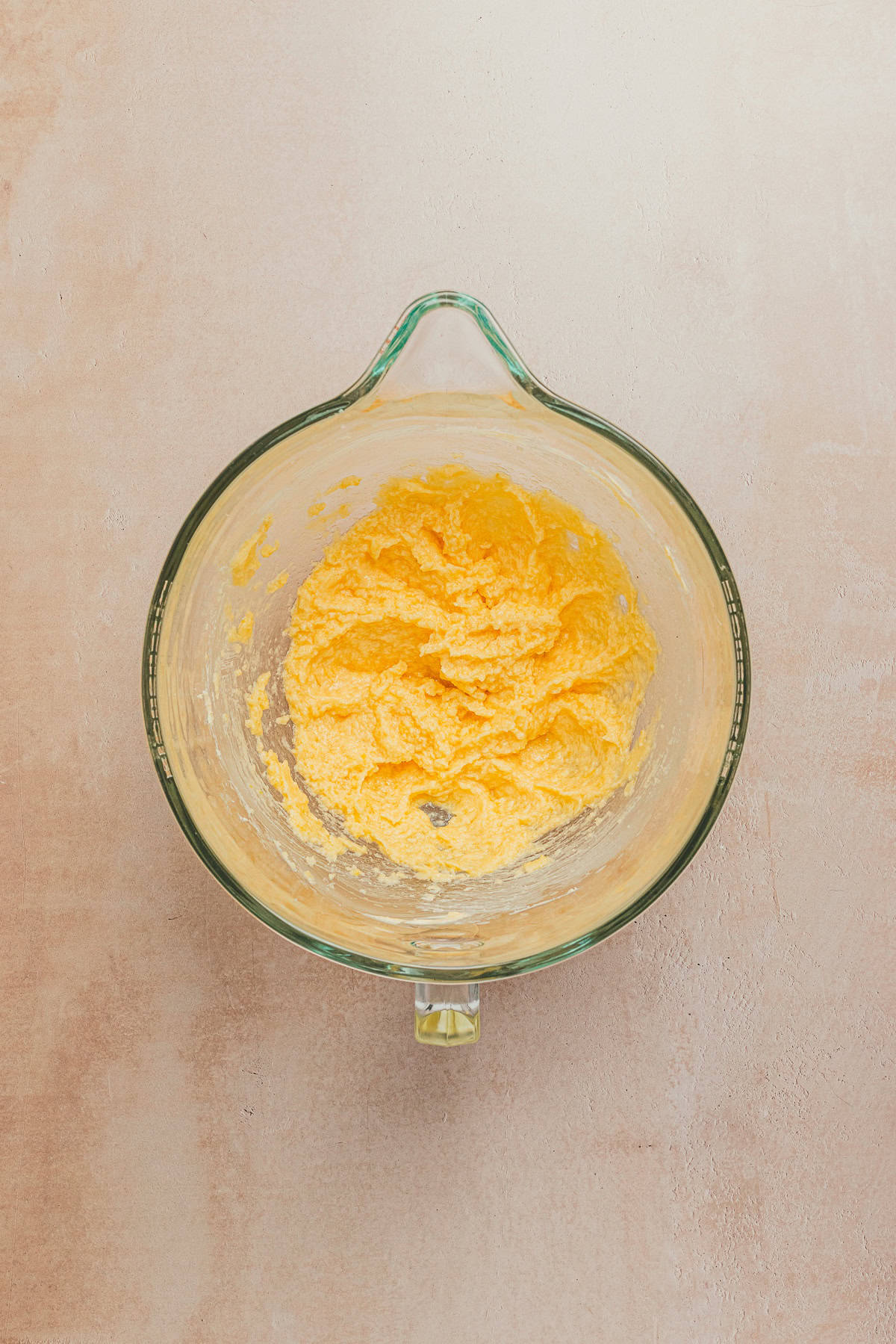 Creamed butter, lemon zest, sugar, egg, and vanilla extract mixture for lemon sandwich cookies in a glass mixing bowl.