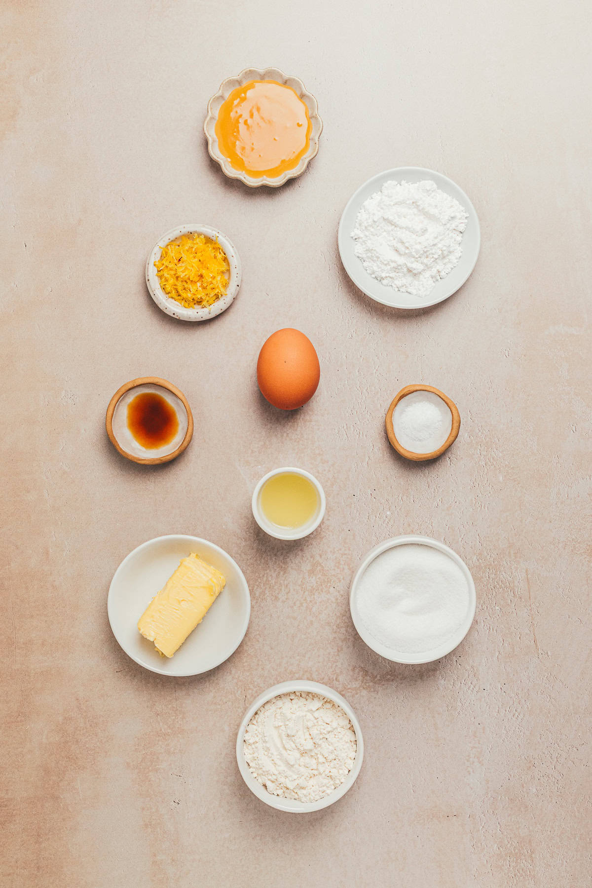 Flat lay of ingredients for lemon sandwich cookies including flour, butter, sugar, powder sugar, egg, butter, lemon curd, lemon zest, lemon juice, and vanilla on a neutral background.