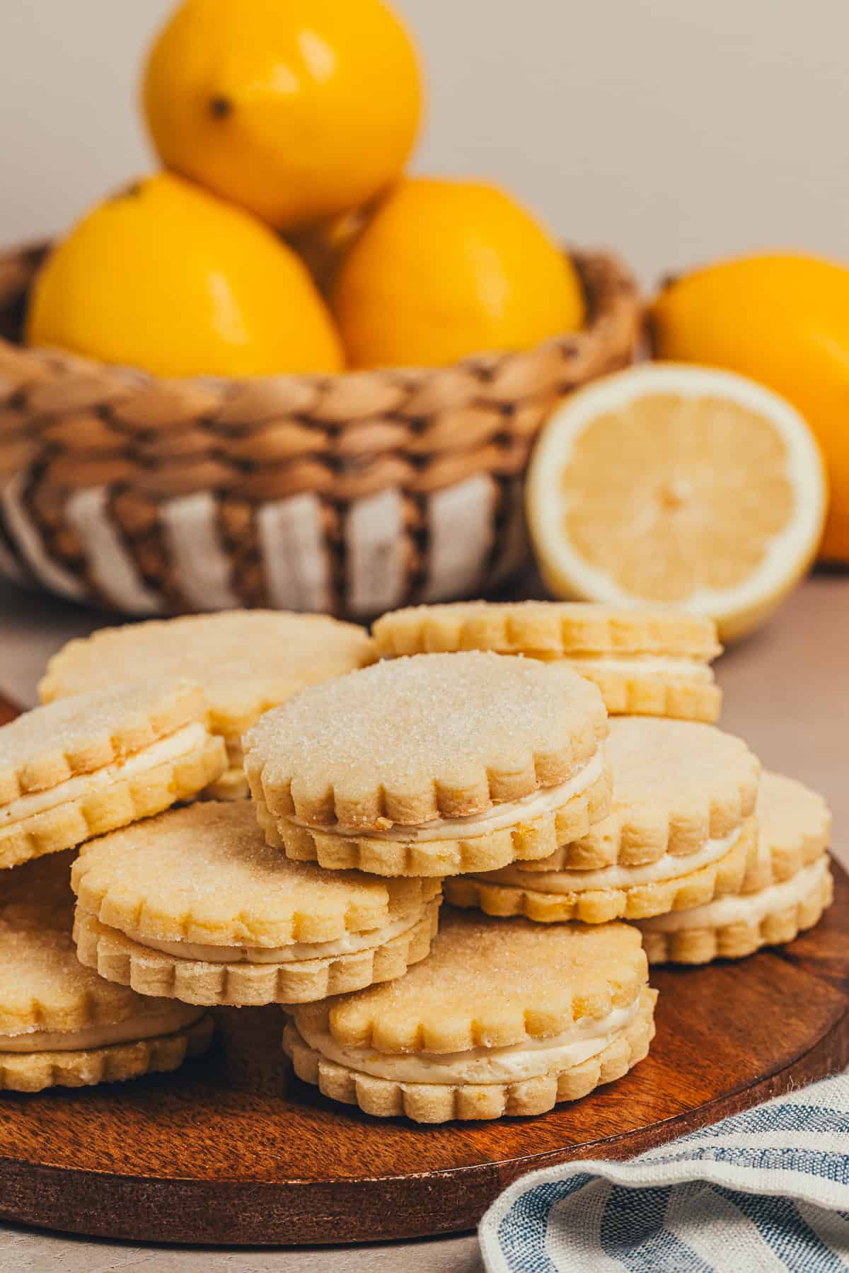 Lemon sandwich cookies with buttercream filling on a wooden board with fresh lemons in the background.