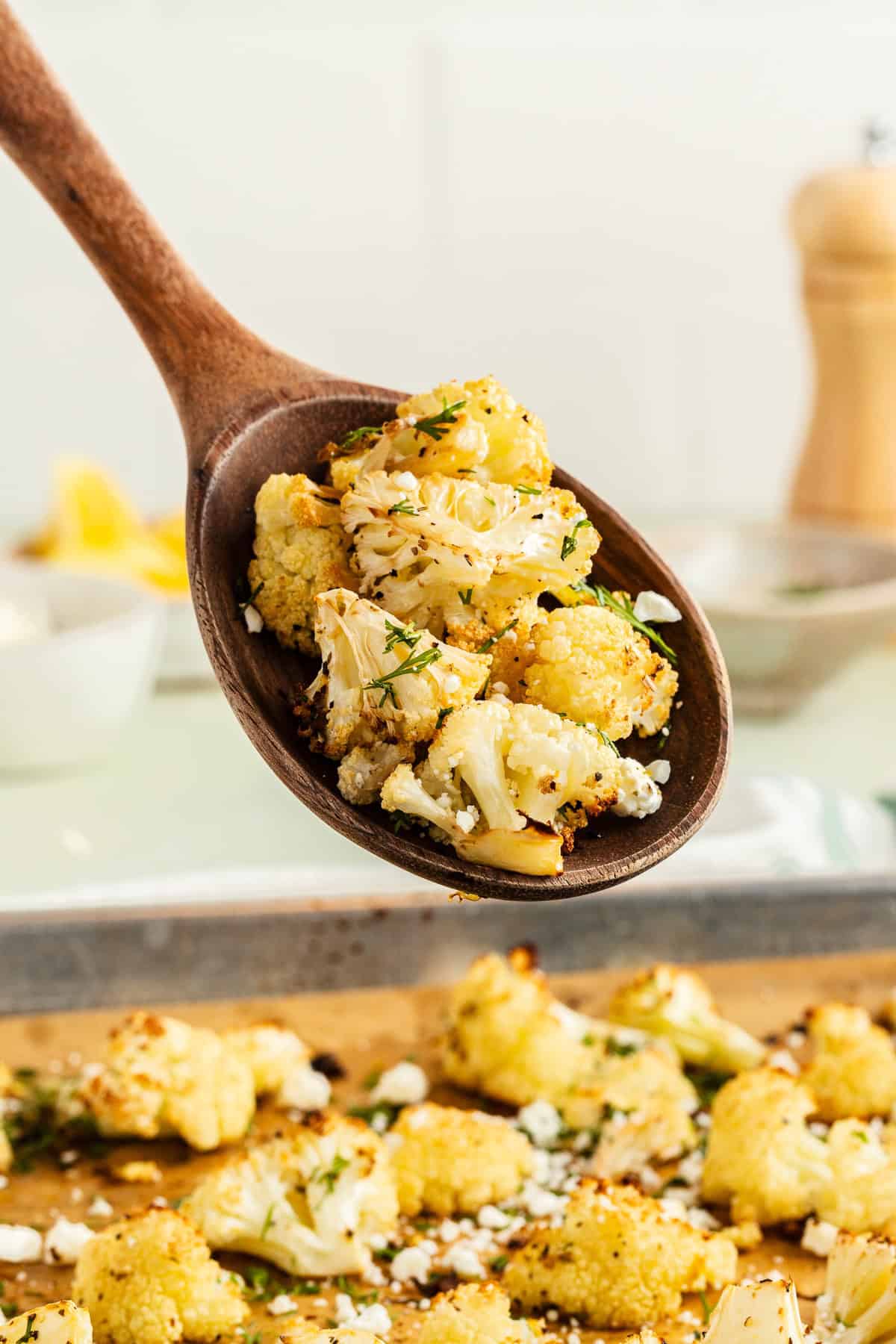 Wooden spoon holding roasted cauliflower with feta and fresh dill.