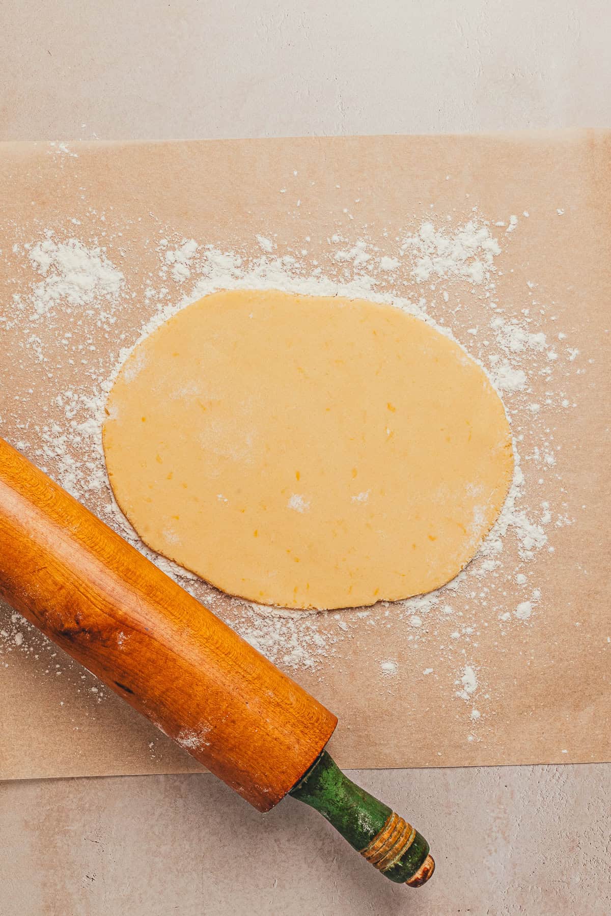 Lemon cookie dough rolled out on a floured surface with a wooden rolling pin.