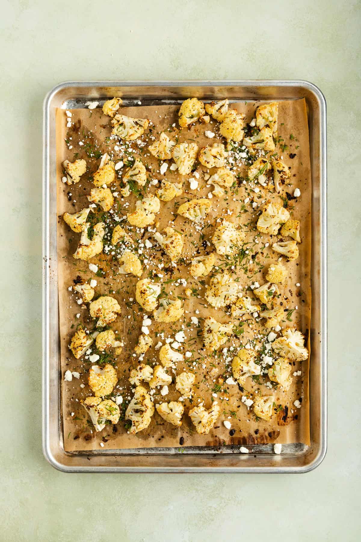 Sheet pan roasted cauliflower with feta and dill garnished with fresh herbs.