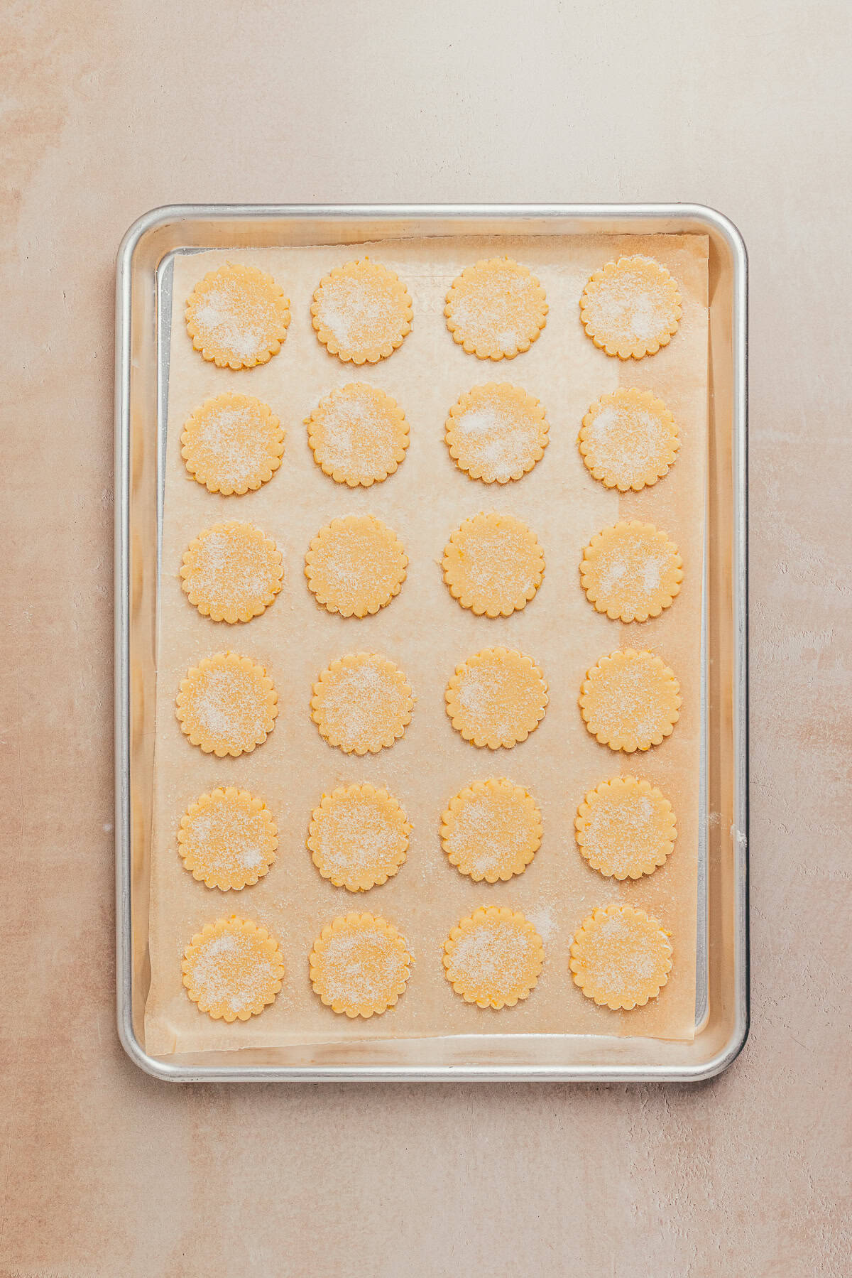Unbaked lemon sandwich cookies with scalloped edges sprinkled with sugar on a parchment-lined baking sheet.