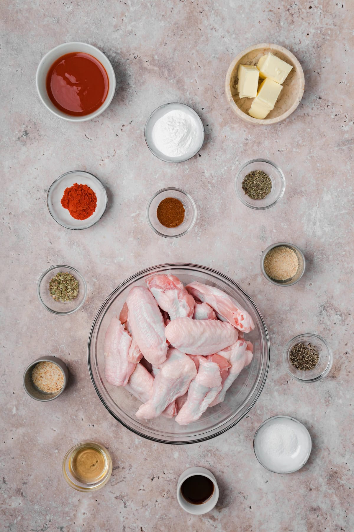 Cajun chicken wings ingredients laid out with raw wings, spices, butter, and hot sauce.