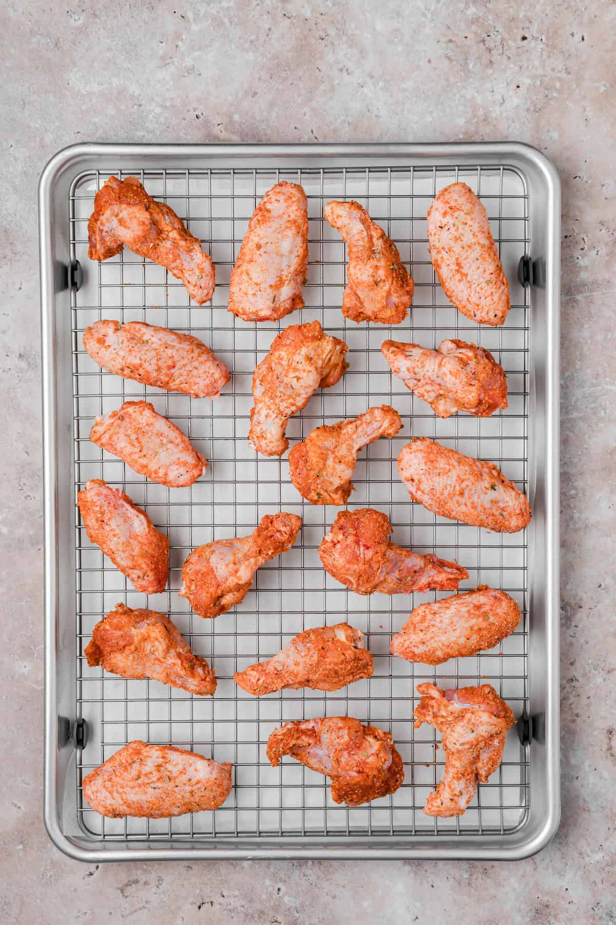 Cajun chicken wings arranged on a wire rack over a baking sheet before cooking.