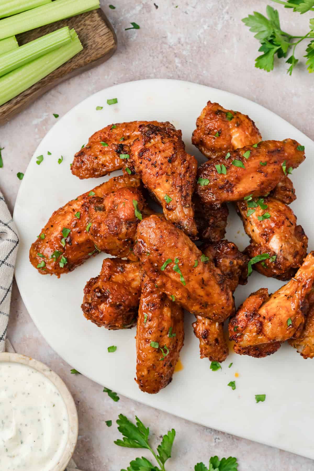 Overhead view of homemade Cajun chicken wings arranged on a plate with fresh herbs and celery nearby.