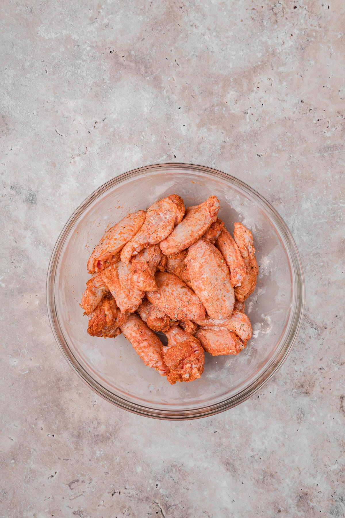 Cajun seasoned chicken wings coated in spice mixture in a glass bowl.