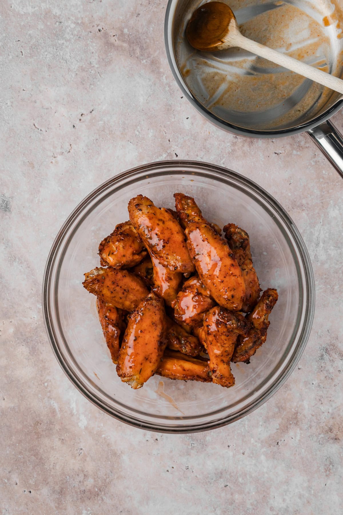 Cajun chicken wings tossed in sauce in a glass bowl with saucepan in background.