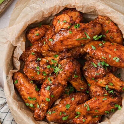 Crispy Cajun chicken wings in a parchment-lined bowl, garnished with fresh herbs.