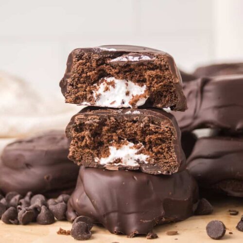 Homemade Ding Dongs with one cut open showing cream filling surrounded by whole chocolate snack cakes and chocolate chips.