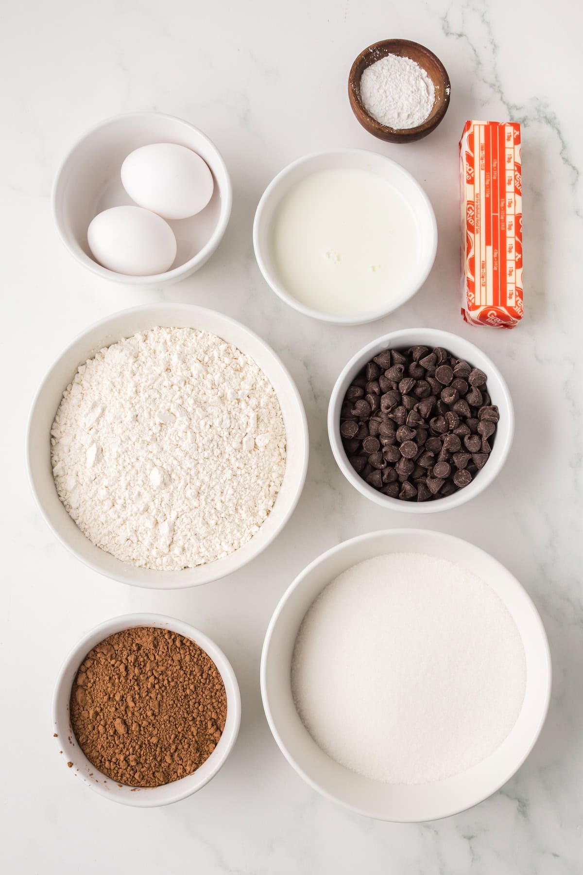 Ingredients for homemade ding dongs including cocoa powder, flour, eggs, sugar, butter, milk, and chocolate chips.