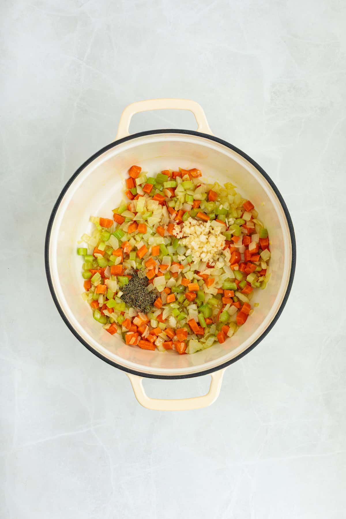 Diced onions, carrots, and celery sautéing with fresh garlic and thyme in a Dutch oven for homemade lemon chicken orzo soup.