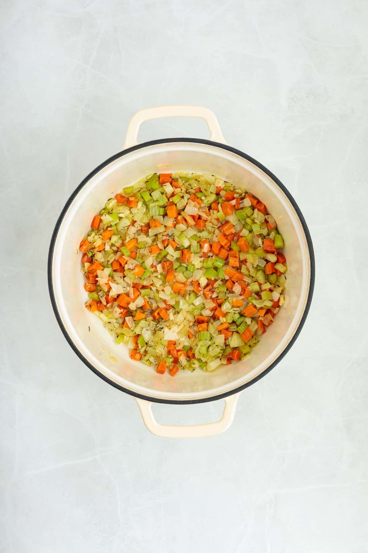 Sautéed onions, carrots, celery, garlic, and herbs cooking in a Dutch oven for homemade lemon chicken orzo soup.