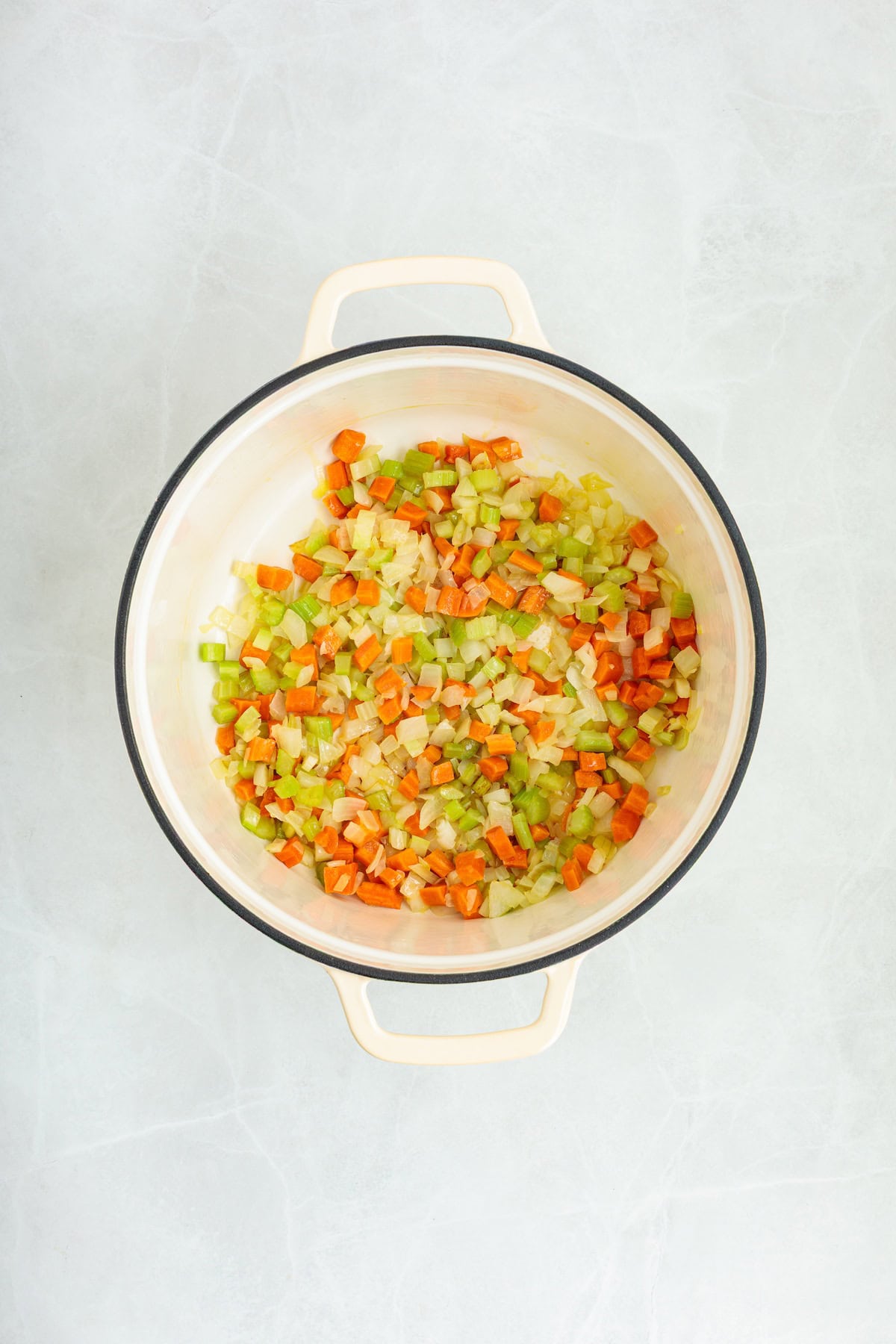 Softened vegetables cooking in a Dutch oven for homemade lemon chicken orzo soup, including onions, carrots, and celery.