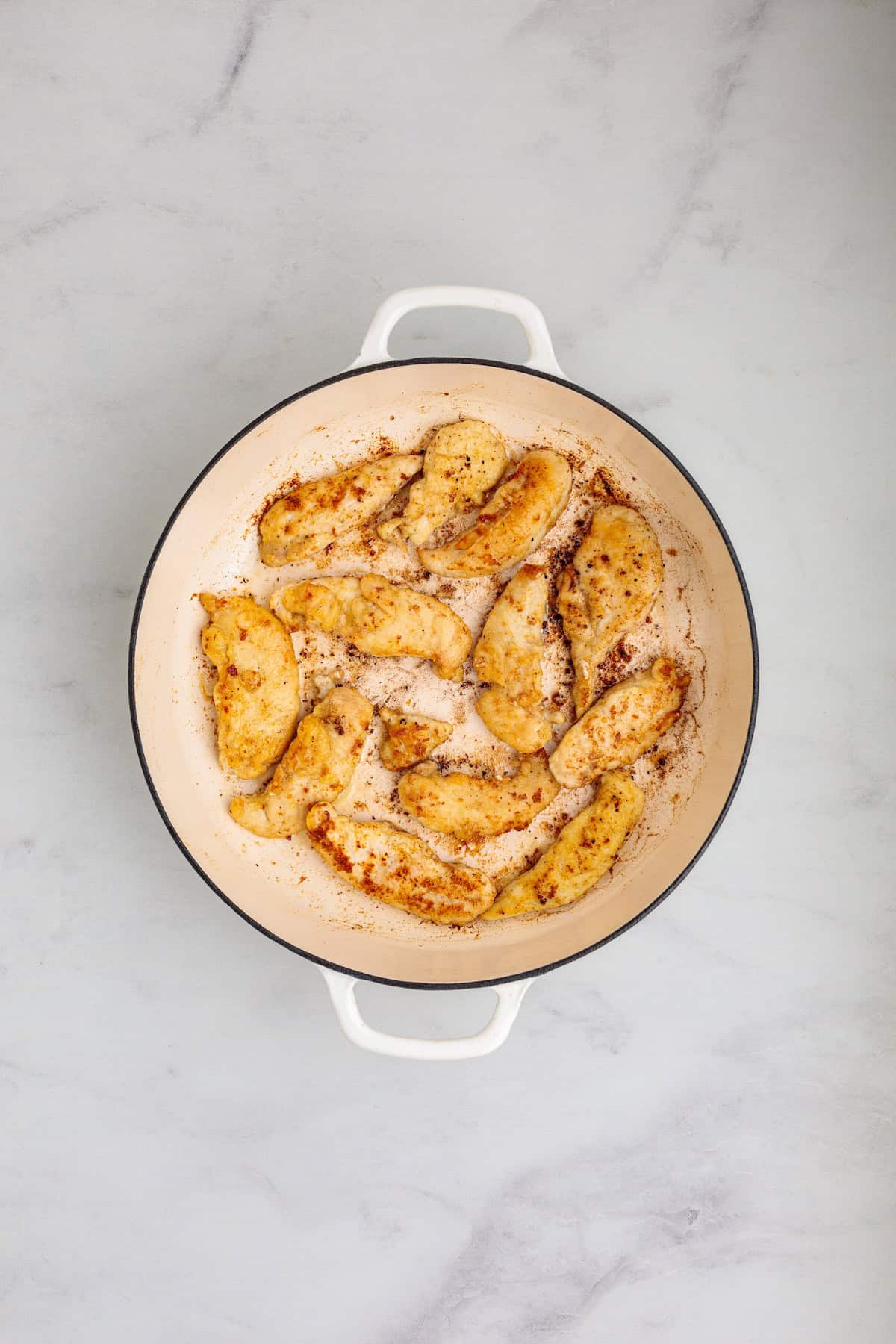 Golden pan-seared chicken tenders cooked in a skillet for creamy chicken Marsala fettuccine with mushroom sauce.